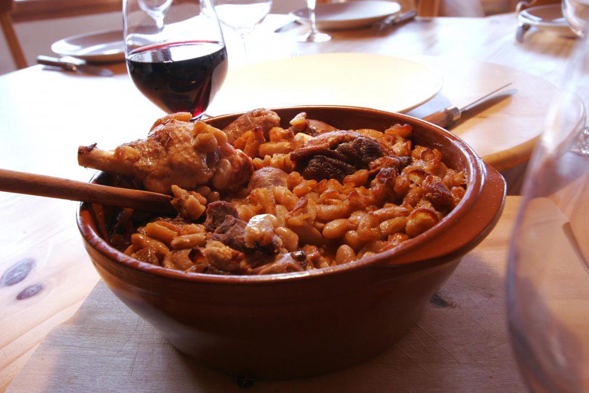 Cassoulet dans son plat en terre cuite, servi à table avec un verre de vin.